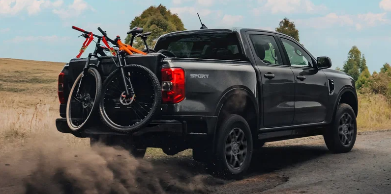 An individual driving down a dirt road with mountain bikes in the back.